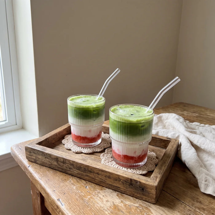 Dvi ledinės braškių matcha latte stiklinės ant medinio padėklo