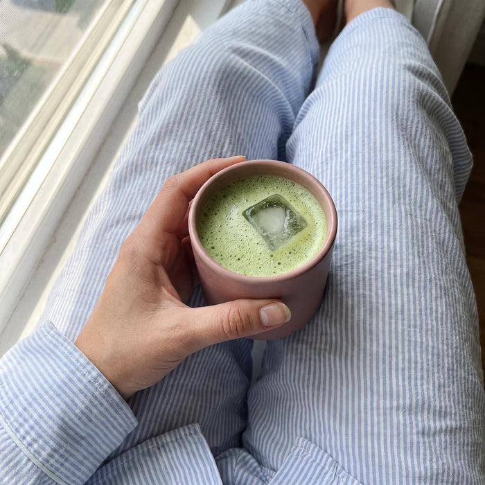 Rausvas puodelis ledinės matcha latte rankoje rytą